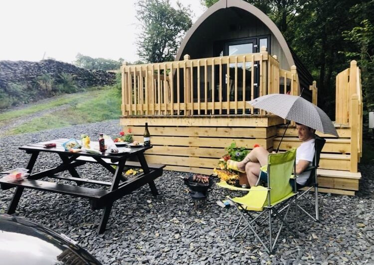 man sat with an umbrella outside glamping pod