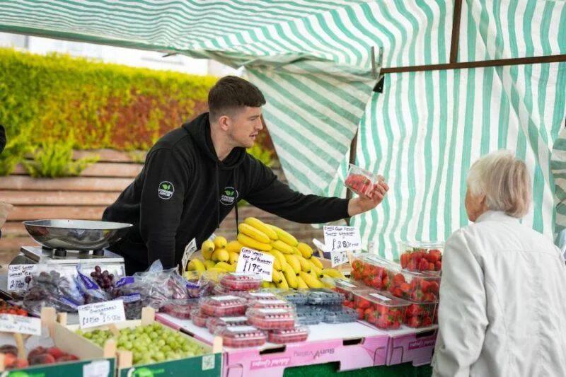 man handing elderly woman strawberries at market
